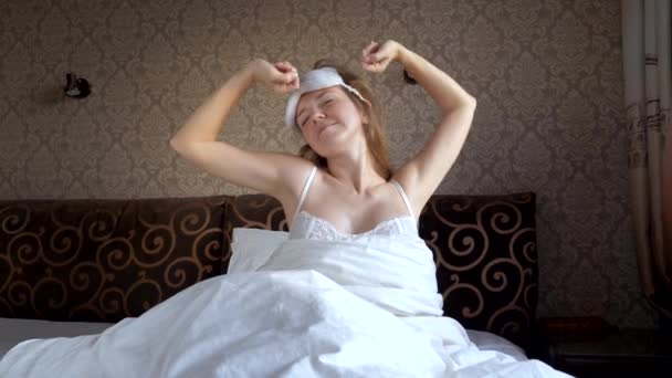 Jonge vrouw met blinddoek Wakes Up, Stretches en glimlachen, zittend in haar bed — Stockvideo