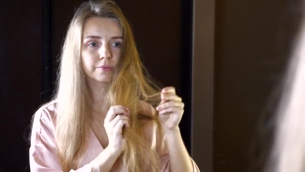 Donna infelice con i capelli secchi e fragili che controllano i suoi capelli aggrovigliati nello specchio — Video Stock