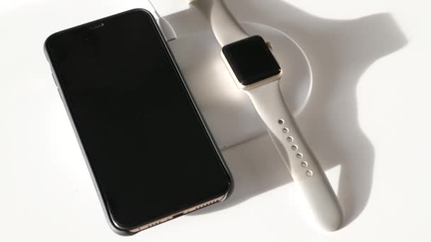 Mobilní telefon a chytré hodinky ležící na nabíjecím panelu pro bezdrátové nabíjení — Stock video