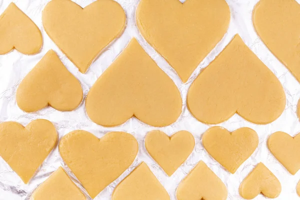 Rauwe zelfgemaakte hartvormige koekjes liggen op bakolie en bereiden zich voor om naar de oven te worden gestuurd — Stockfoto