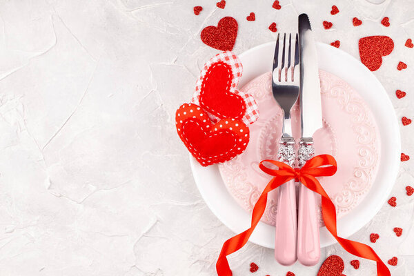 Белые и розовые тарелки с вилкой, ножом и красной лентой лук с декоративными сердцами
