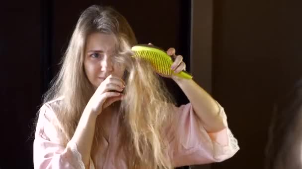 Несчастная женщина с сухими хрупкими волосами, проверяющая свои запутанные волосы в зеркале — стоковое видео