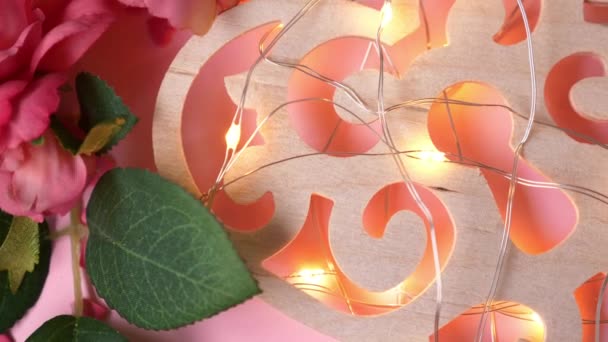 Houten Hart met Lichten slinger Leugens op Roze Achtergrond met Harten en Bloemen — Stockvideo