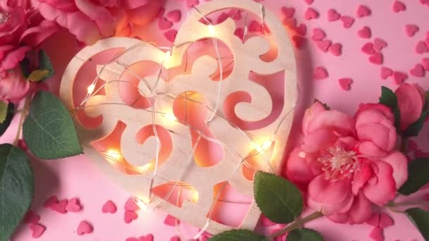 Holzherz mit Lichterkranz liegt auf rosa Hintergrund mit Herzen und Blumen