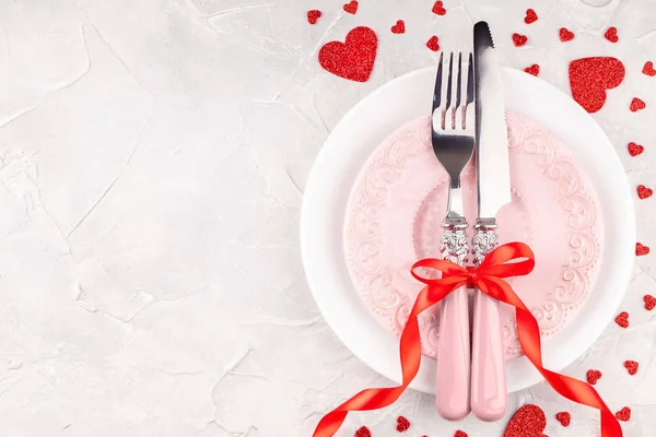 Witte en roze borden met vork, mes en rode linten strik met decoratieve harten — Stockfoto