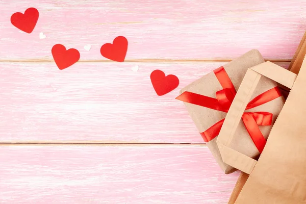 Craft papírový sáček a dárkové balení s červenou stuhou luk a srdce na růžovém pozadí — Stock fotografie