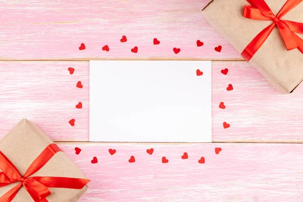 Bílá prázdná karta se dvěma dárkovými krabicemi s stuhou na růžovém dřevěném pozadí — Stock fotografie