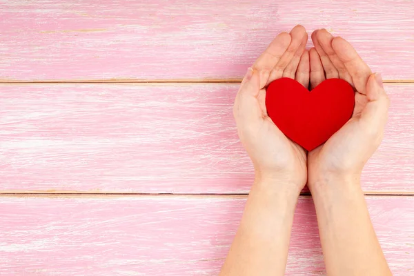 Kobieta Ręce Trzymając Czerwone Serce na Różowym Drewnianym Tło - Opieka zdrowotna, Miłość — Zdjęcie stockowe