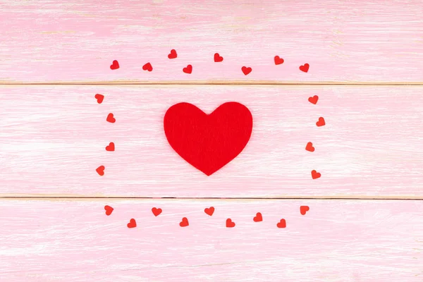 Kleine Confetti Harten op roze houten achtergrond met rood hart in het centrum — Stockfoto