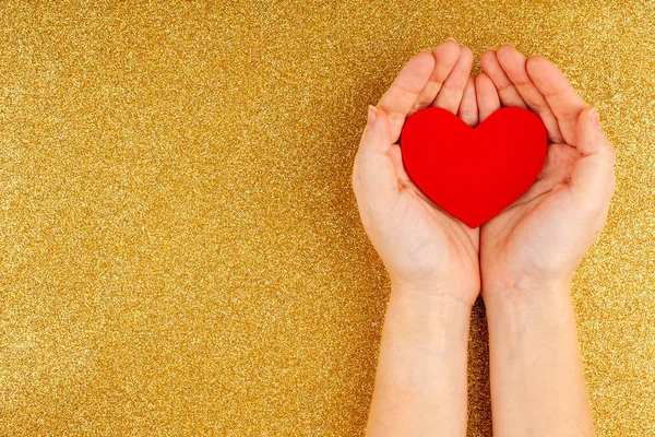 Manos de mujer sosteniendo el corazón rojo sobre fondo dorado - Salud, Amor — Foto de Stock