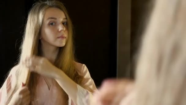 Junge hübsche Frau schaut in den Spiegel und trägt Öl auf ihre langen Haare auf — Stockvideo