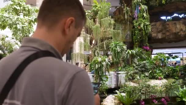 Hombre caucásico se para con un teléfono en sus manos en un moderno centro comercial — Vídeo de stock