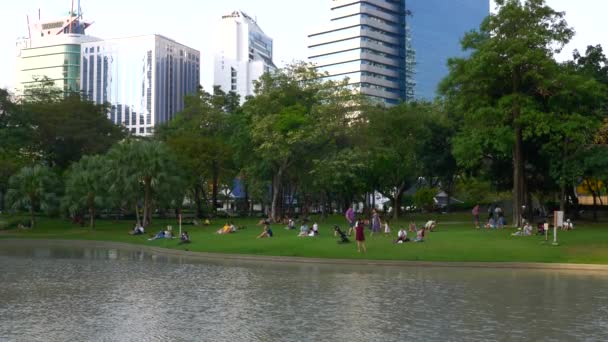 Gente Relájese en Parque Público con Lago y Árboles Verdes con Edificios de Rascacielos — Vídeo de stock