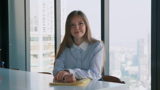 Glimlachende jonge zakenvrouw zit alleen op kantoor en kijkt naar camera — Stockvideo