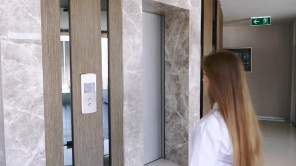 Молодая деловая женщина нажав кнопку "Лифт" в офисном центре — стоковое видео