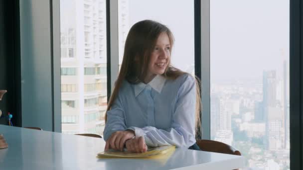 Посміхаючись молода бізнес-леді сидить в офісі і дивиться на камеру — стокове відео