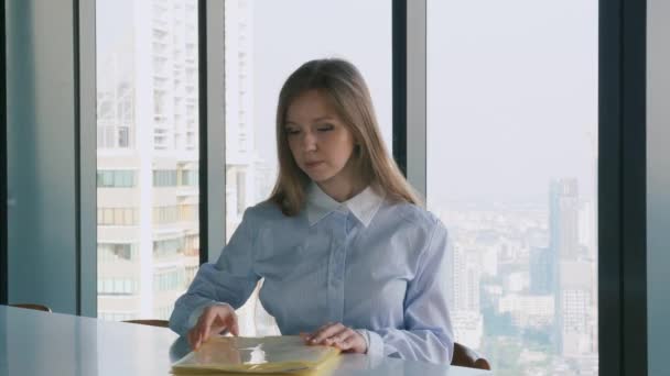 Mujer de negocios con carpeta con documentos en el escritorio cerca de la ventana con vista a la ciudad — Vídeo de stock