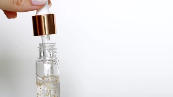 Serum mit Goldtropfen, die aus der Kosmetikpipette auf weißem Hintergrund fallen — Stockvideo