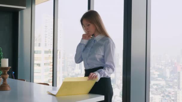 Бизнесмен, стоящая в современном офисе, размышляющая о работе и держащая папку — стоковое видео