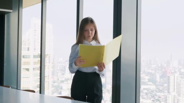 Mujer de negocios sosteniendo la carpeta con documentos cerca de la ventana con vista a la ciudad — Vídeo de stock