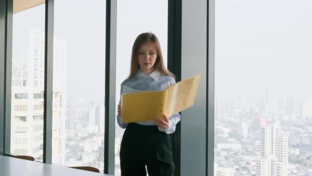 Mujer de negocios sosteniendo la carpeta con documentos cerca de la ventana con vista a la ciudad — Vídeo de stock
