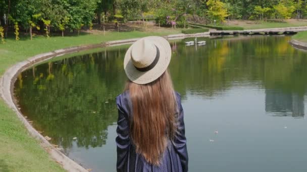 Hasır Şapkalı Kadın Arka Görünümü Gölün yanında duruyor ve Doğanın tadını çıkarıyor — Stok video