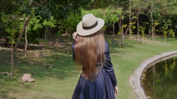 Toeristische Vrouw met strohoed Wandelen langs het meer in Summer Tropical Park — Stockvideo