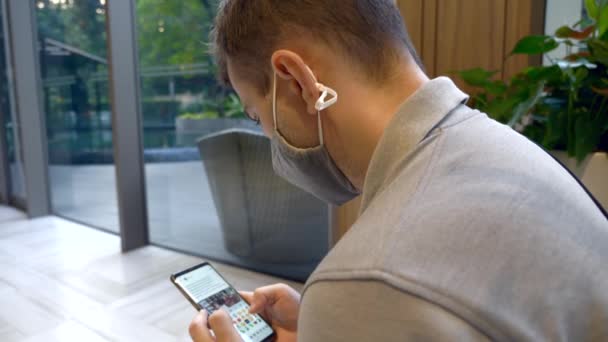 Vista Lateral del Hombre Joven en la Máscara de Salud Cara Usando Smartphone — Vídeo de stock