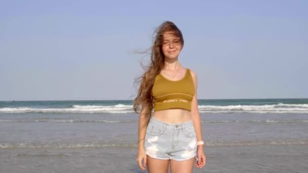 Mosolygós gyönyörű lány hosszú haj áll a strandon, és keres a kamera — Stock videók