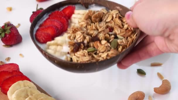 Frau legt Hand in Hand eine natürliche Schüssel mit Bio-Müsli, Banane und Erdbeere — Stockvideo