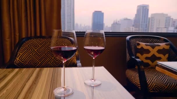 Két üveg vörösbor stand az asztalon, este város a háttérben — Stock videók