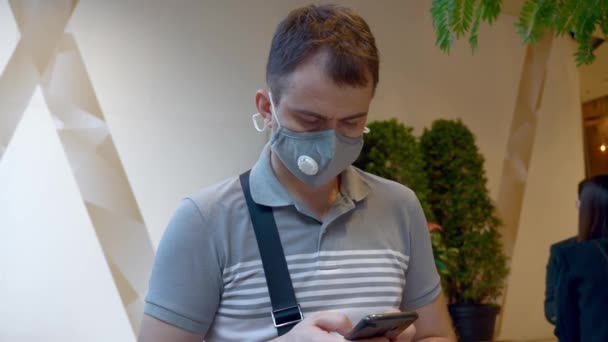 Man in Health Face Mask Stand w Hall of Business Building Użyj smartfona — Wideo stockowe