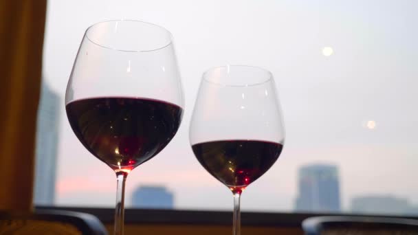 Δύο ποτήρια κόκκινο κρασί σταθεί στο τραπέζι με το βράδυ της πόλης στο παρασκήνιο — Αρχείο Βίντεο