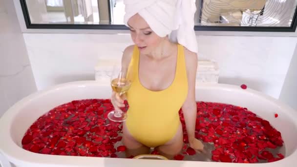 Mujer sexy en traje de baño con vino blanco Relájese en la bañera con pétalos de flores — Vídeo de stock