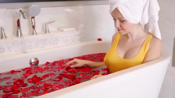 Attraente giovane donna con asciugamano sulla testa Prendendo un bagno pieno di petali di rosa — Video Stock