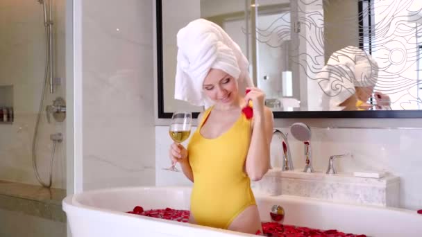 Glücklich lächelnde junge Frau badet mit Rosenblättern und hält Champagnerglas in der Hand — Stockvideo