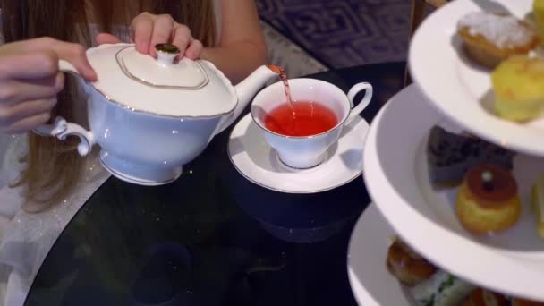 Frau gießt roten Tee aus einer Vintage-Teekanne in weiße Tasse — Stockvideo