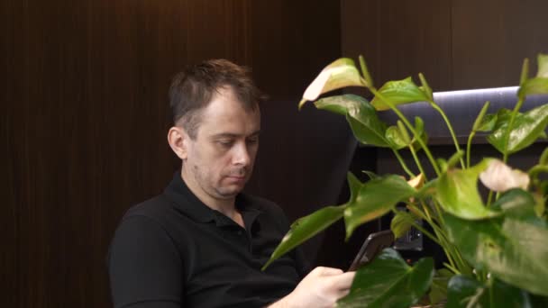 Европейский человек сидит в кафе за чашкой кофе и смотрит новости на своем телефоне — стоковое видео