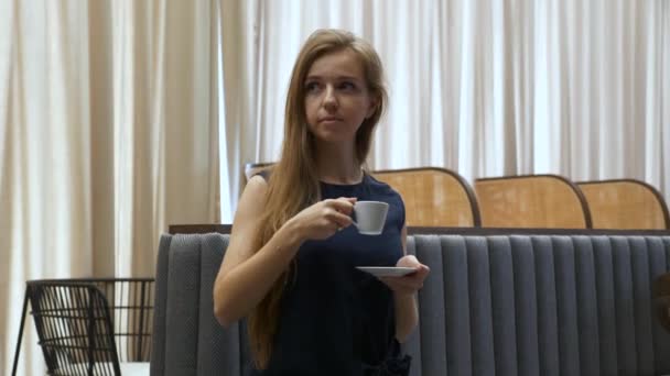 Mujer hermosa sonriente sentada en el sofá en Café, tomar una taza de café de la mesa — Vídeo de stock