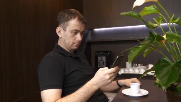Ο άνθρωπος κάθεται στην καφετέρια και χρησιμοποιώντας το κινητό του τηλέφωνο, βλέποντας τις ειδήσεις — Αρχείο Βίντεο