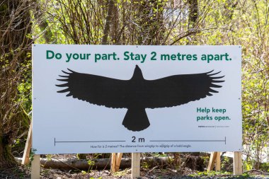 Kel bir kartalın kanat açıklığını kullanarak sosyal mesafeyi arttırmak için iki metreyi gösteren bir işaret. 14 Nisan 2020 Vancouver BC Kanada