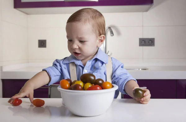 Baby boy playing with ripe colorful cherry tomatoes — Stock Photo, Image