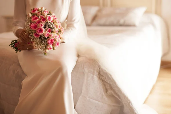 Bride sitting in the bed holding the bouquet in the white colore — Stock Photo, Image