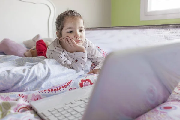 Little girl watching movies with a laptop. Looks distracted — Stock Photo, Image