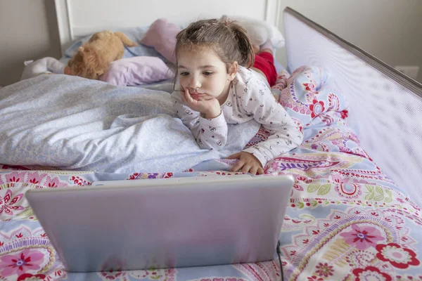 Niña viendo películas con un portátil en la cama — Foto de Stock