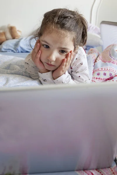 Little girl watching films with a laptop. She looks attentive — Stock Photo, Image