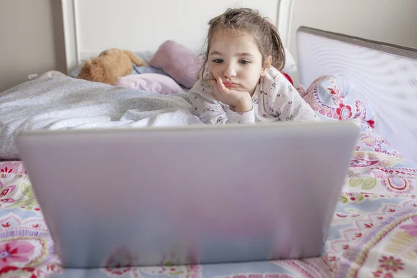 Liten flicka titta på filmer med en bärbar dator i sängen — Stockfoto