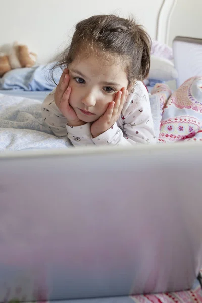 Liten flicka titta på filmer med en bärbar dator. Hon ser uppmärksam — Stockfoto