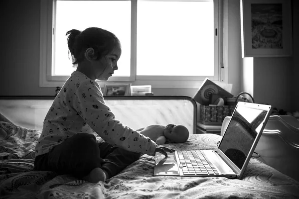 Liten flicka sitter i sängen och spela spel med laptop pc — Stockfoto