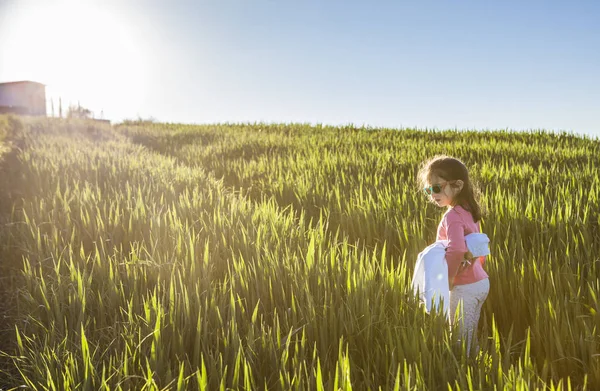 Menina e sua boneca andando através do campo de cereais verde em s — Fotografia de Stock